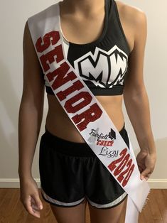 a woman in a sports bra top and shorts with a sash around her waist, standing on a hard wood floor