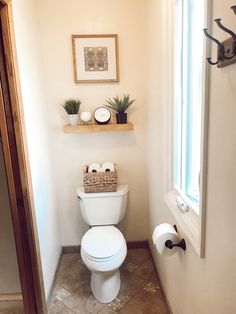 a white toilet sitting in a bathroom next to a window with potted plants on top of it