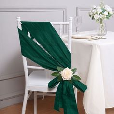 a white rose sits on the back of a chair at a table with green sashes