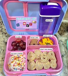 a pink lunch box filled with food on top of a marble counter next to a purple container