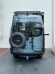 the back end of a blue van parked in a parking lot next to a building