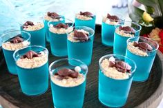 there are many desserts in glasses on the tray with blue liquid and chocolate toppings