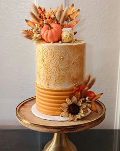 a three tiered cake decorated with fall leaves and sunflowers on a wooden stand