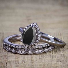 two wedding rings with black and white diamonds on top of each other, sitting on a piece of wood