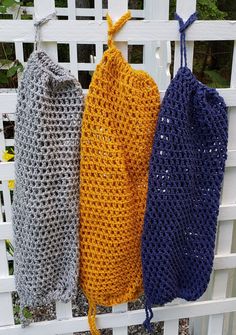 three crocheted bags hanging on a white fence