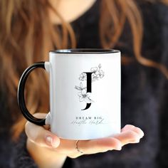 a woman is holding a coffee mug with the letter j on it and flowers all over it