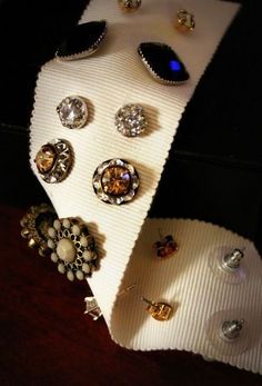 an assortment of jewelry is displayed on a white cloth with black and gold buttons in the center