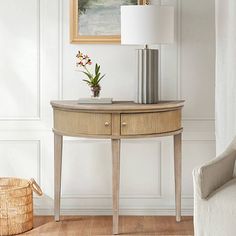 a small table with a lamp on it next to a white chair and a painting