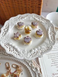 some cookies are sitting on a white plate next to an open book and cupcakes