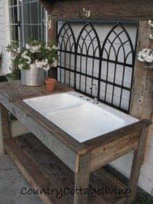 a sink sitting on top of a wooden table next to a window and potted plants