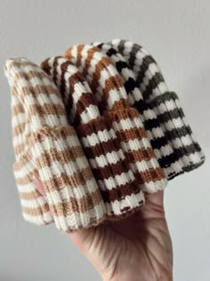 the hand is holding three knitted hats