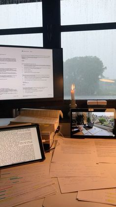 there are many papers on the desk with an electronic device next to it and a candle