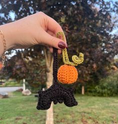 a hand holding an orange and black crocheted keychain in the shape of a pumpkin