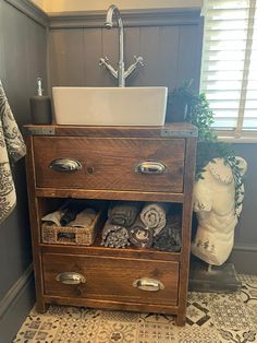 a bathroom sink sitting next to a wooden cabinet with drawers and towels on top of it