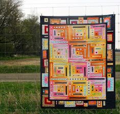 a quilt hanging on a wire fence in a field with grass and trees behind it