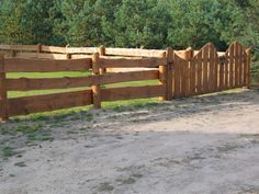 a wooden fence in the middle of a dirt road next to some grass and trees