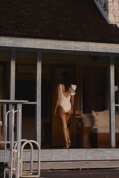 a woman in a white bodysuit is walking out of a house with an open door