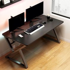 a computer desk with two monitors and a keyboard on it in front of a window