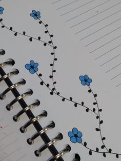 an open spiral notebook with blue flowers and black pins on the cover, sitting on a table