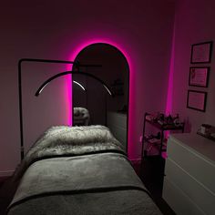 a dimly lit room with a bed, dresser and pink light on the wall behind it