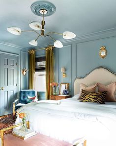 a bedroom with blue walls and white bedding, gold accents on the headboard