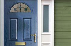 a blue front door with a gold handle on the side and green house behind it