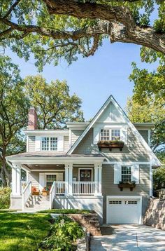 a white and gray house with lots of trees in the front yard on a sunny day