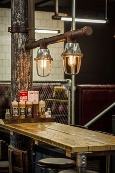 some lights hanging over a wooden table in a room with stools and tables around it