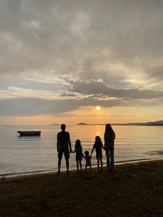 a group of people standing on top of a beach next to the ocean at sunset