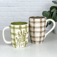 two coffee mugs sitting next to each other on a white table with a brick wall in the background