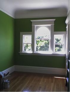 an empty room with green walls and white trim on the windows, hardwood flooring