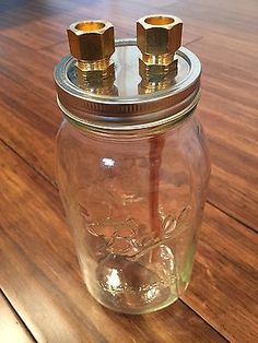 a glass jar with two brass knobs sitting on top of a wooden table