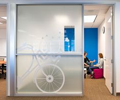 two people are sitting in an office with bikes etched on the glass wall behind them