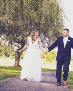 a bride and groom holding hands while walking down a path in front of a tree