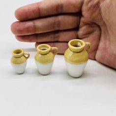 three small white and yellow vases sitting next to each other in front of a person's hand