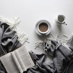 a cup of coffee and an open book on a white table with gray blankets around it