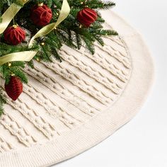 a christmas tree skirt with red balls and gold ribbons on it's edge, next to a white knitted sweater