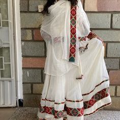 a woman standing in front of a brick wall wearing a white dress with red and green accents