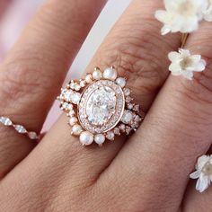 a close up of a person's hand with a ring on it and flowers in the background