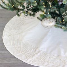 a christmas tree skirt with snowflakes and ornaments on the bottom is shown in front of a white round tablecloth