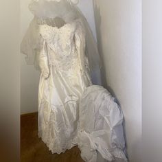 a white wedding dress and veil on display in a corner next to a wall with a wooden floor