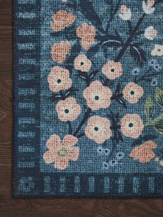 a blue rug with orange and pink flowers on the front is sitting on a wooden floor