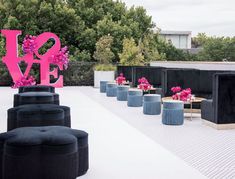 an outdoor event with black couches and pink flowers on the top floor, surrounded by trees