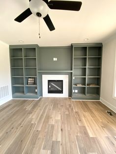 an empty living room with wood floors and gray bookcases on either side of the fireplace