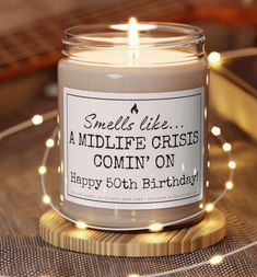 a candle is sitting on a table with some lights around it that says, smells like a midlife crisis comin'on happy 50th birthday