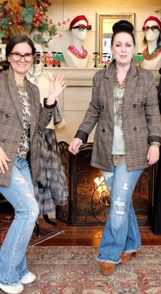 two women standing in front of a fireplace with christmas decorations on the mantle behind them