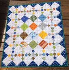 a quilted table topper with many different colors and designs on it, sitting on a wooden surface