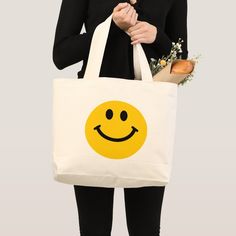 a woman holding a tote bag that has a smiley face on it and flowers