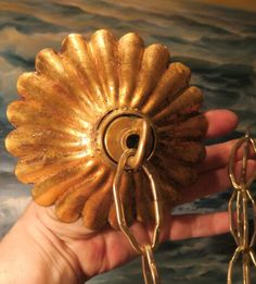 a hand holding a golden flower shaped object with chains attached to it's side