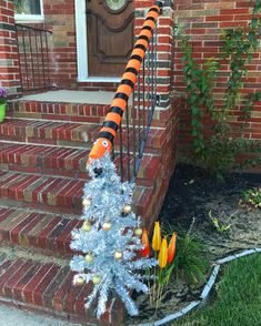 a decorated christmas tree on the steps of a brick house with an orange and black striped fish decoration